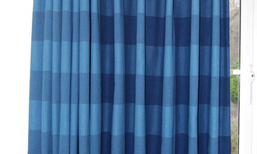 Photo of curtain in blue checked fabric with curtain half open and half closed to show effect on the design