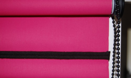 Photograph of a roller blind in a bright pink plain fabric with black piping along bottom bar